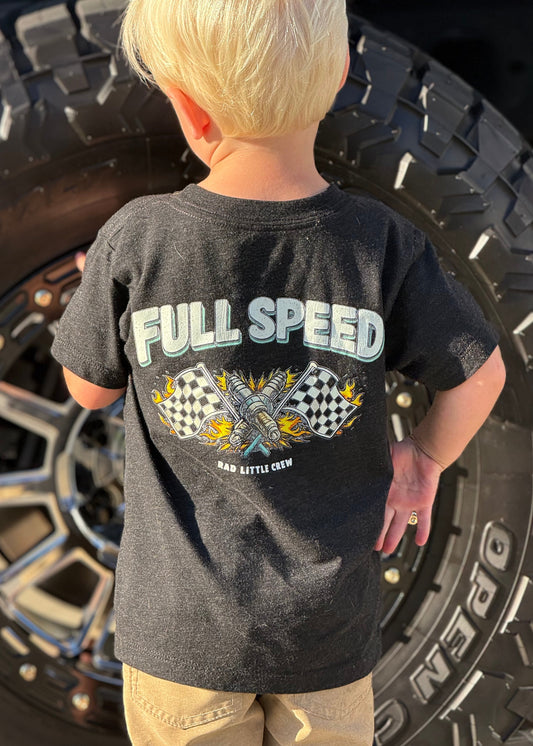 Child wearing a 'Full Speed' t-shirt standing in front of a large tire.