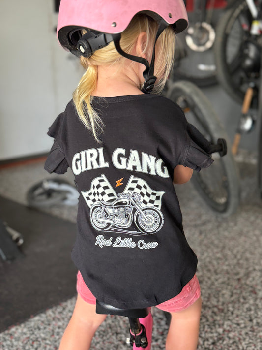 Child wearing a black t-shirt with 'Girl Gang' and motorcycle graphic, standing in a garage.